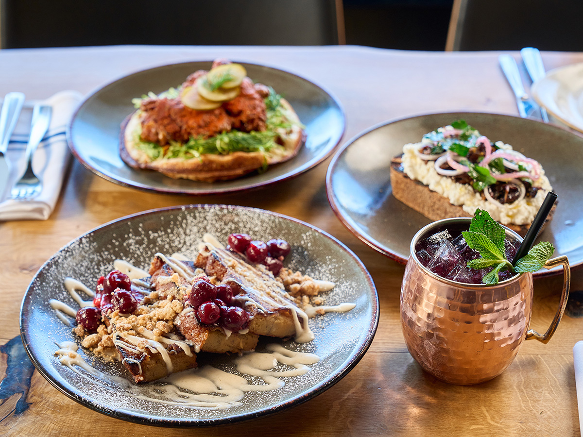 Three brunch dishes on a table - french toast, chicken and waffles, and mushroom toast 